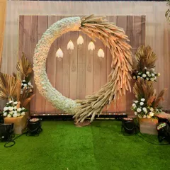 For a bohemian-themed event, I designed this photo booth using a large circular wreath made of white flowers and dried pampas grass. The backdrop is a rustic wooden panel, and the hanging tulip-shaped lights add a touch of whimsy.
