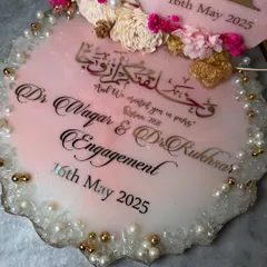 A close-up of the personalized engagement tray, showing the elegant Arabic calligraphy and the couple's names. The edges are finished with a crystal-like resin and delicate pearls.