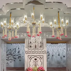 An elegant reception hall entrance featuring grand chandeliers adorned with jasmine and rose garlands. The walls are decorated with intricate mirror work and jaali patterns, creating a luxurious and traditional welcome.