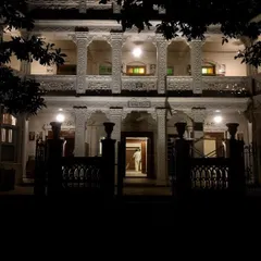The inner courtyard of Rhodesia House at night, viewed from the entrance. The restored columns and balconies create a dramatic play of light and shadow, hinting at the layers of history contained within its walls and inviting exploration.