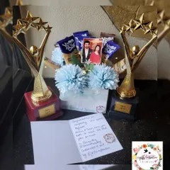 A gift combo featuring two custom trophies and a bouquet made of healthy Yoga Bars and flowers, celebrating 700 episodes of a show.