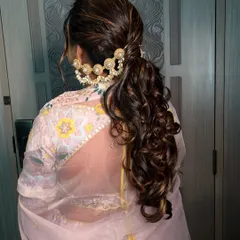 A chic and modern ponytail with soft curls and a statement pearl hair accessory. This hairstyle is perfect for a sangeet or reception look.
