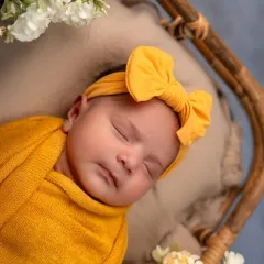 A close-up portrait of the baby in her yellow wrap and bow. These shots highlight the sweet, delicate features of your newborn, from their button nose to their tiny lips.
