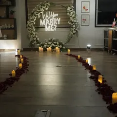 I create unforgettable romantic moments with setups like this surprise proposal. A candlelit path strewn with rose petals leads to a beautiful floral ring and a "Will You Marry Me?" neon sign, perfect for a terrace or indoor proposal.