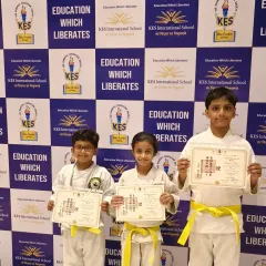 Three young karatekas from KES International School proudly display their new yellow belts and certificates. This is a significant first step in their martial arts training, marking their official entry into the world of karate.