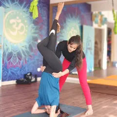 A TTC student receives guidance on assisting with an inversion, a crucial skill for any aspiring yoga teacher.
