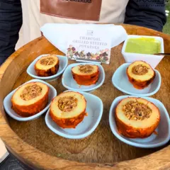 Charcoal Grilled Stuffed Potatoes served in individual dishes on a wooden tray. This appetizer offers a smoky flavor and a hearty filling, presented with a side of green chutney.