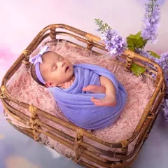 A perfect little bundle. This newborn is peacefully asleep in a rustic basket, surrounded by soft textures and delicate lavender flowers.