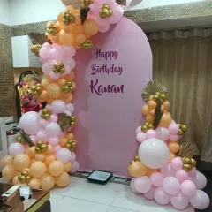 A warm and inviting birthday setup with a pink arched backdrop. The balloon garland in peach, pink, and gold tones adds a touch of elegance to this home decoration.