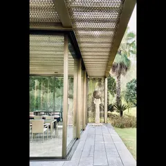 A side view of the glass pavilion, showing its slender steel frame and the seamless transition to the surrounding lawn. The design is an exercise in structural minimalism.