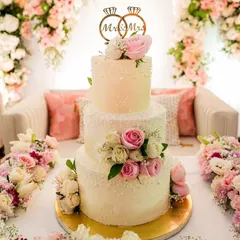 A closer look at this elegant three-tiered wedding cake. The design features delicate pearl-like details, a custom ring topper, and is beautifully arranged with fresh roses, creating a timeless and romantic centerpiece.