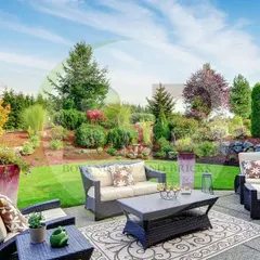 This spacious backyard combines a paved patio area for outdoor furniture with a large, open lawn surrounded by mature trees and shrubs. It's a perfect example of a functional family garden designed for both relaxation and recreation.