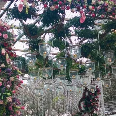 A close-up of a floral arch, showing the intricate details of the arrangement. Hanging glass tea light holders and crystal strings are nestled among the flowers, adding a delicate sparkle.