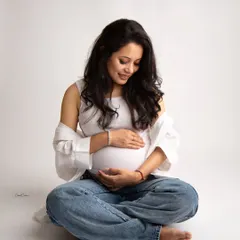 A beautiful, candid-style moment. The mom-to-be looks down at her bump with a sweet smile, her casual outfit perfect for this intimate portrait.