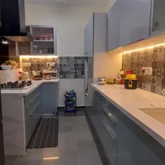 A sleek parallel kitchen with glossy grey cabinets and handle-less drawers. The design is complemented by patterned backsplash tiles and under-cabinet LED lighting, creating a bright and modern cooking environment.