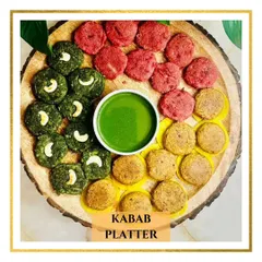 A colorful and appetizing Kebab Platter featuring hara bhara kebabs topped with cashews, vibrant beetroot kebabs, and galouti kebabs, all centered around a fresh mint chutney.