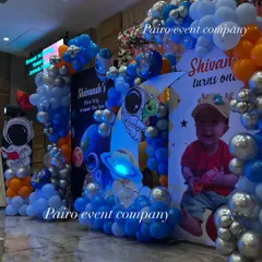 A full view of the Space theme stage, featuring an astronaut, planets, a custom photo backdrop, and arches made of blue, orange, and silver balloons.
