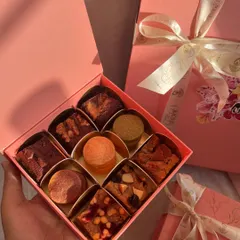 A close up of my mini assortment box, held in hand to show its perfect gifting size. You can see the different textures of the brownies, blondies, and shortbread cookies, all nestled in their golden tray.