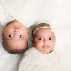 A simple and sweet portrait of two wide-eyed twins. Posed on a soft white blanket, their connection and individual personalities shine through.