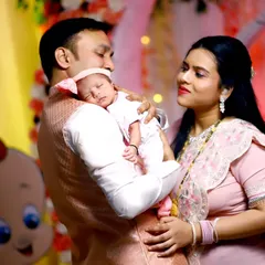 A tender family portrait from a naming ceremony. The father holds their sleeping newborn while the mother looks on with love, creating a warm and intimate photograph.