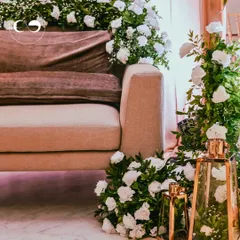 A close-up of the main seating area for a Roka, adorned with cascades of white roses and baby's breath. The gold lanterns add a touch of warm, ambient light to the elegant setup.