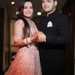 A classic couple portrait from their engagement function. They are holding hands and smiling at the camera, capturing the happiness of the moment in their beautiful traditional outfits. This is a timeless shot for any family album.