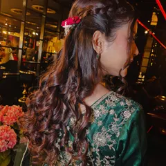 A detailed view of the party hairstyle. This braided half-up, half-down style with loose curls is a versatile and popular choice for festive occasions, adorned here with a small flower.