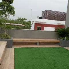 A minimalist rooftop garden in GK1 featuring a clean patch of artificial lawn next to a wooden deck. A long, low-profile wooden bench is integrated into the design, providing simple and functional seating.