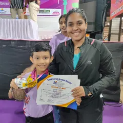A proud coach stands with one of our national-level champions. He is holding his certificate and medals after winning multiple prizes in floor gymnastics and vault at a recent competition.