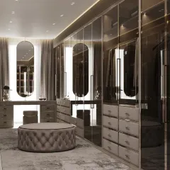 This closet design exudes a moody and sophisticated vibe with smoked glass doors and a dark color scheme. A plush, tufted ottoman sits at the center, providing a comfortable spot for dressing.