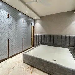 A modern bedroom centered around a grey color palette. The vertical stitching on the upholstered bed back is complemented by the clean lines of the chevron pattern on the wardrobe doors.
