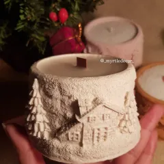 A closer look at our 'Winter Lights' jar candle, held in hand to show its comforting size and intricate, snowy cabin details. We pour these 100% soy wax candles ourselves, making them a perfect piece of warmth for any cozy corner or as a thoughtful Christmas gift.