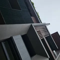 A detail shot of a facade featuring brutalist architectural elements. The design combines the raw texture of exposed concrete with treated wood and sleek aluminum louvers, demonstrating our ability to create earthy yet sophisticated exteriors.