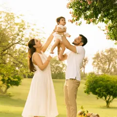 Parents lift their baby girl up towards a flowering tree, all three sharing a moment of pure joy. This image uses the beauty of nature to frame a perfect, happy family interaction.