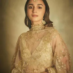 Alia Bhatt in a full-length view, showcasing the complete bridal or festive look. The handcrafted earrings, maang tika, and delicate bracelet in 18k gold and pearls complement her embroidered lehenga perfectly.