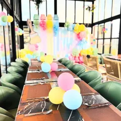 A view down the long guest table at the art-themed party, with small balloon clusters as centerpieces. In the background, the main paint-themed backdrop creates a colorful and exciting focal point for the celebration.