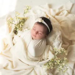 This newborn girl looks like a little flower bud, nestled in a white bowl with delicate baby's breath. The all-white, minimalist setup creates a feeling of purity and serenity.