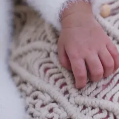 A macro shot of a newborn's hand resting on a textured blanket, emphasizing the smallness and perfection of their fingers.