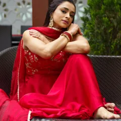 A beautiful portrait from a professional shoot. The makeup features a defined, smokey eye and a neutral lip, creating a sophisticated look that complements the vibrant red anarkali.