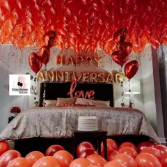 A classic and highly requested anniversary room setup featuring a dense canopy of red ceiling balloons. The bed is the focal point, framed by 'Happy Anniversary' and 'love' foil balloons, creating an intensely romantic atmosphere.