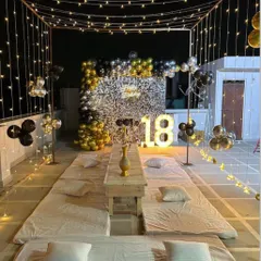 A sophisticated 18th birthday party on a terrace. The setup includes low seating, a sequin wall with a balloon garland, and a beautiful canopy of string lights.