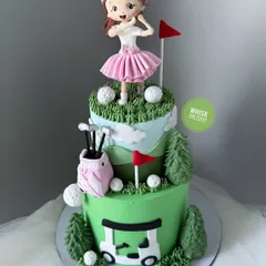 A hole-in-one of a cake for a golf player. This two-tiered cake is decorated with a golf course theme, including a handcrafted female golfer, a golf cart, and clubs.