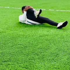 A player performs a focused leg stretch on the turf. This type of static stretching is vital for post-training recovery, helping to increase flexibility and reduce muscle soreness.