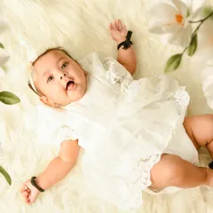 An angelic overhead portrait of a baby girl in a white lace outfit. The simple white flowers add a delicate and natural touch to this newborn-style photo.