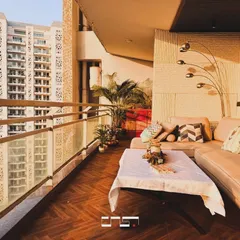 A sun-drenched balcony at the DLF Belaire site, designed for ultimate relaxation. The large L-shaped sofa, herringbone wood flooring, and city views make it a perfect spot to unwind.