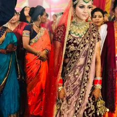 A beautiful bride on her wedding day, wearing a deep maroon velvet lehenga with intricate gold embroidery. This complete bridal look, including the double dupatta, is available for rent.