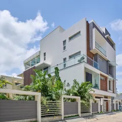 The facade of the 'Wilasa' villa uses a clean, minimalist palette with plaster finishes and vertical wooden slats. The design carefully balances solid surfaces to shield from harsh sun while providing expansive glass balconies.