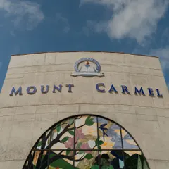 The main entrance facade of Mount Carmel, featuring exposed concrete and a large stained-glass mural. This combination of raw materiality and artistry sets the tone for the creative and spiritual ethos of the educational space within.