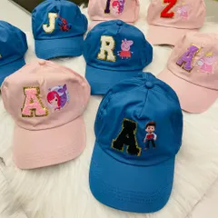 A collection of custom initial caps made as return favors for a kids' party. The image displays a mix of blue and pink caps with patches of characters like Peppa Pig, Paw Patrol, and Spiderman.