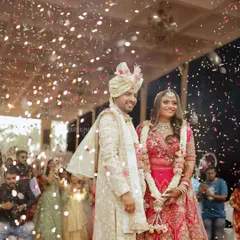 The happy couple stands together during their varmala ceremony, surrounded by guests and a festive shower of confetti.